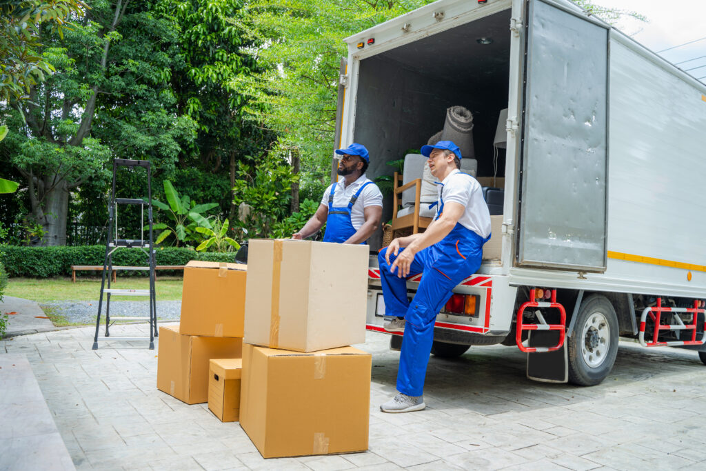 Removal company workers unloading Boxes From Truck Into New Home On Moving Day.